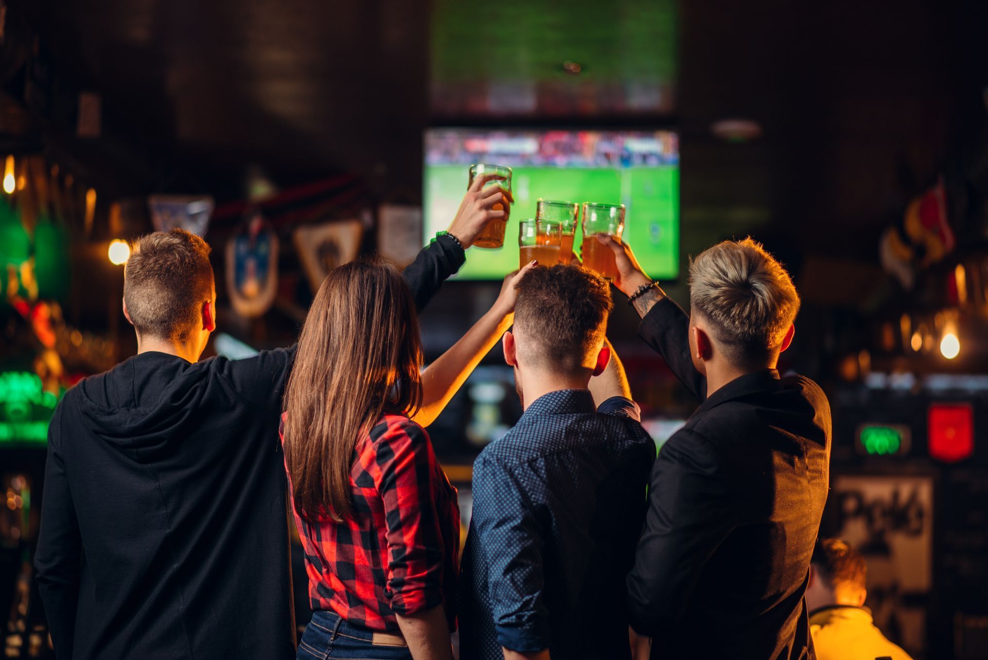 People cheering in a bar, watching a football game on multiple screens, arms raised in celebration.