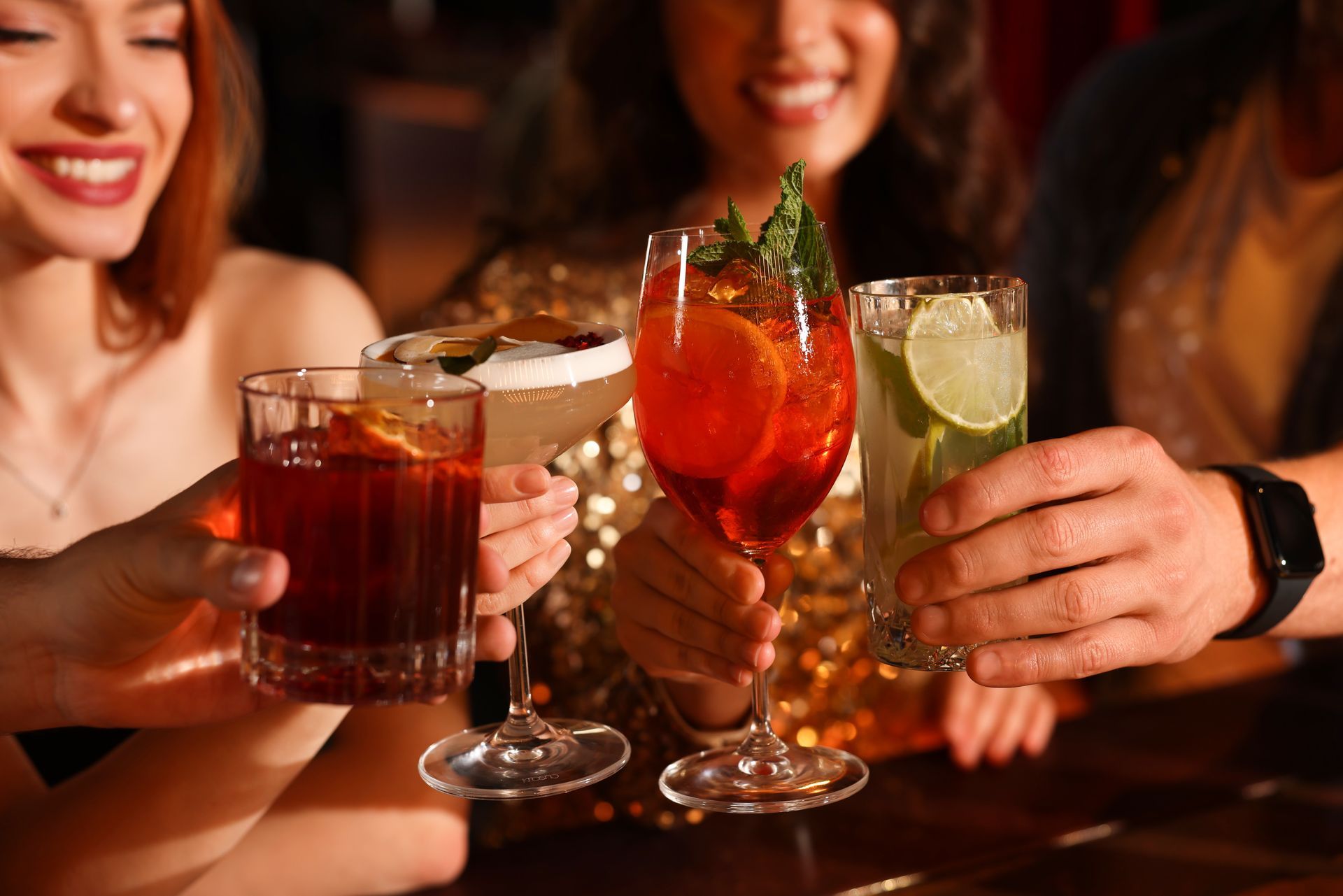 Friends clinking colorful cocktails at a bar, with smiling faces and warm lighting