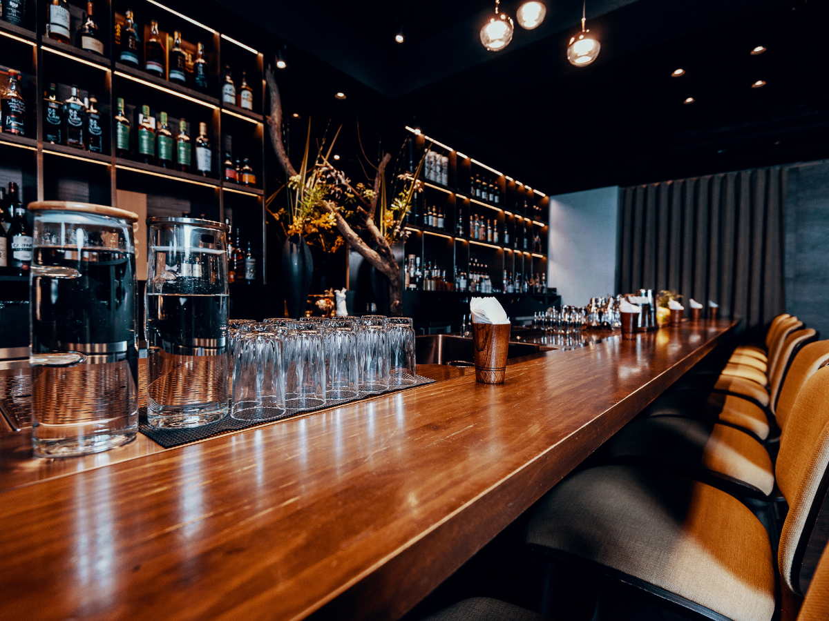 A long wooden bar in a restaurant with a lot of glasses on it.