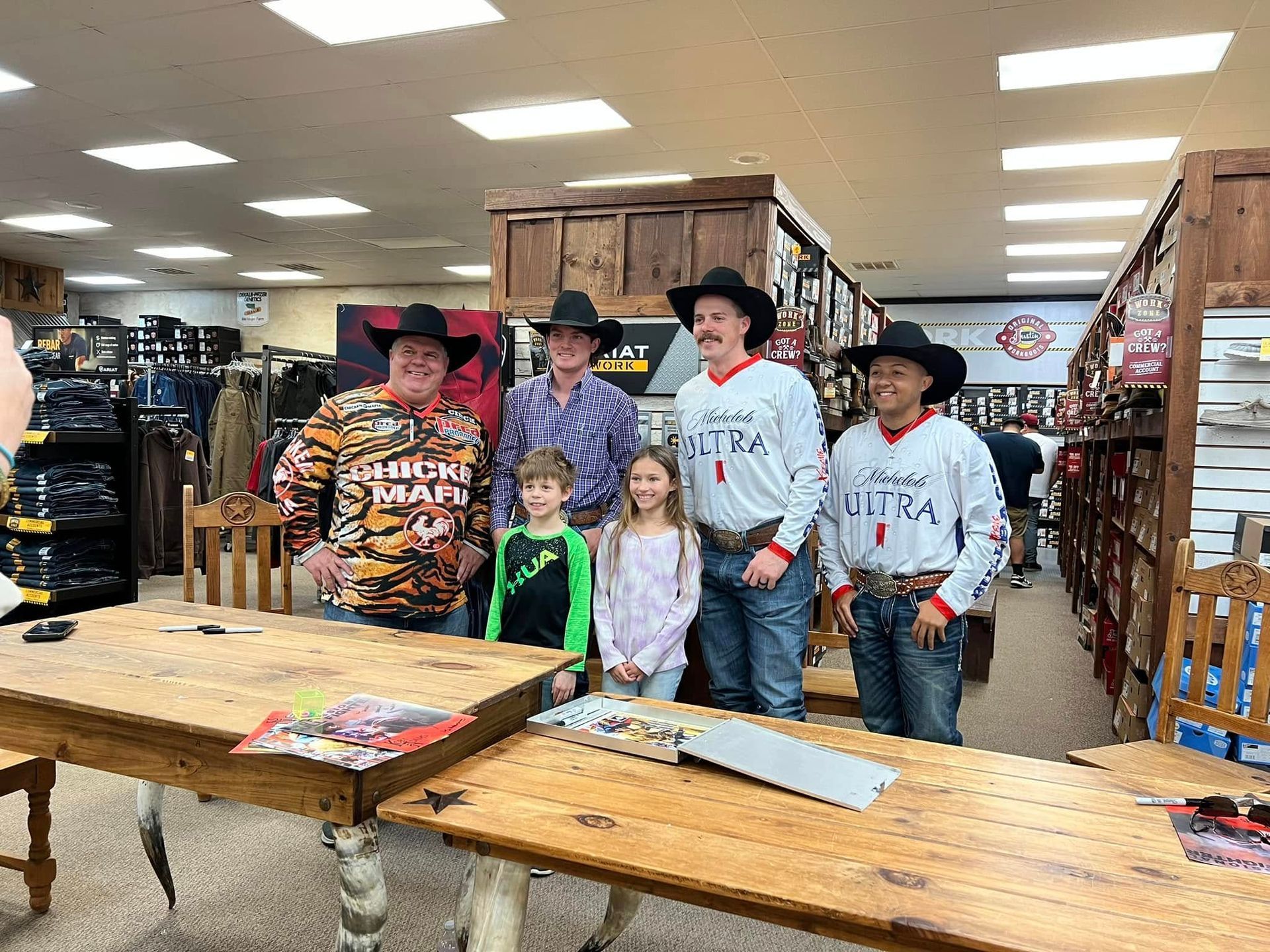 Group of people, including children, in a store with cowboys. Some wear cowboy hats and belts.