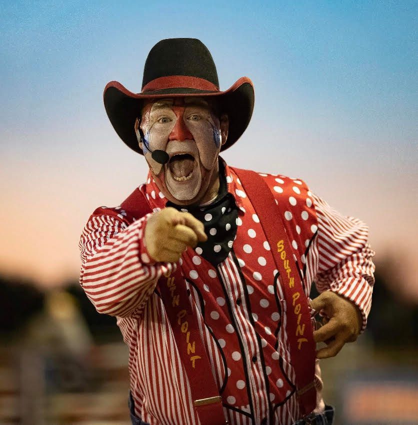 Clown in red and white polka dot attire and cowboy hat, pointing and shouting, outdoors.