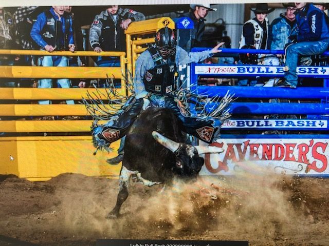 A bull rider in black gear, rides a bucking bull in an arena, dust flying.