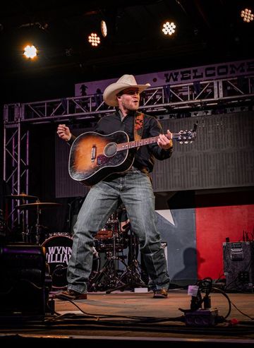Man in cowboy hat plays acoustic guitar on stage, singing.