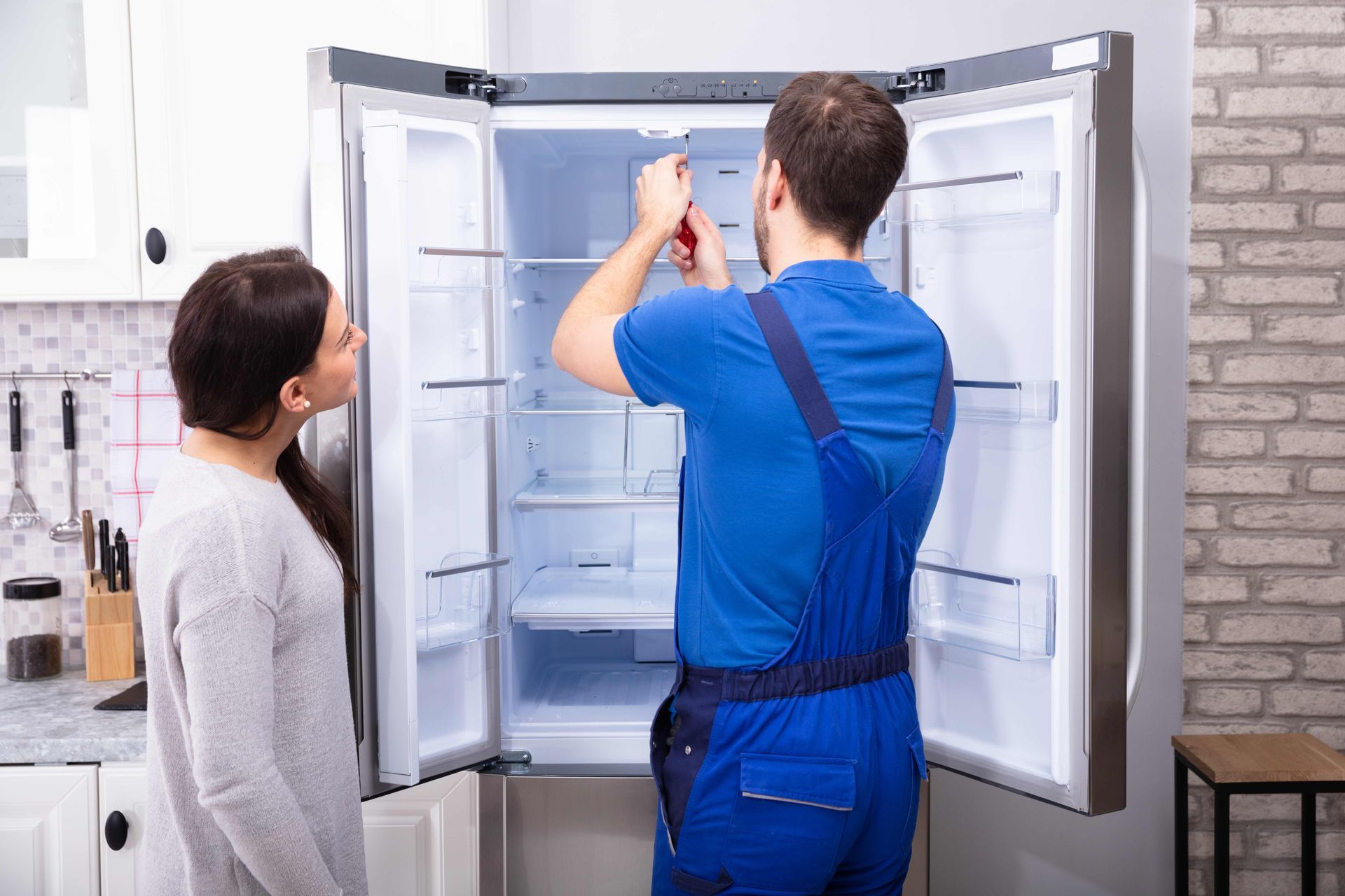 a man is fixing a refrigerator in a kitchen while a woman looks on
