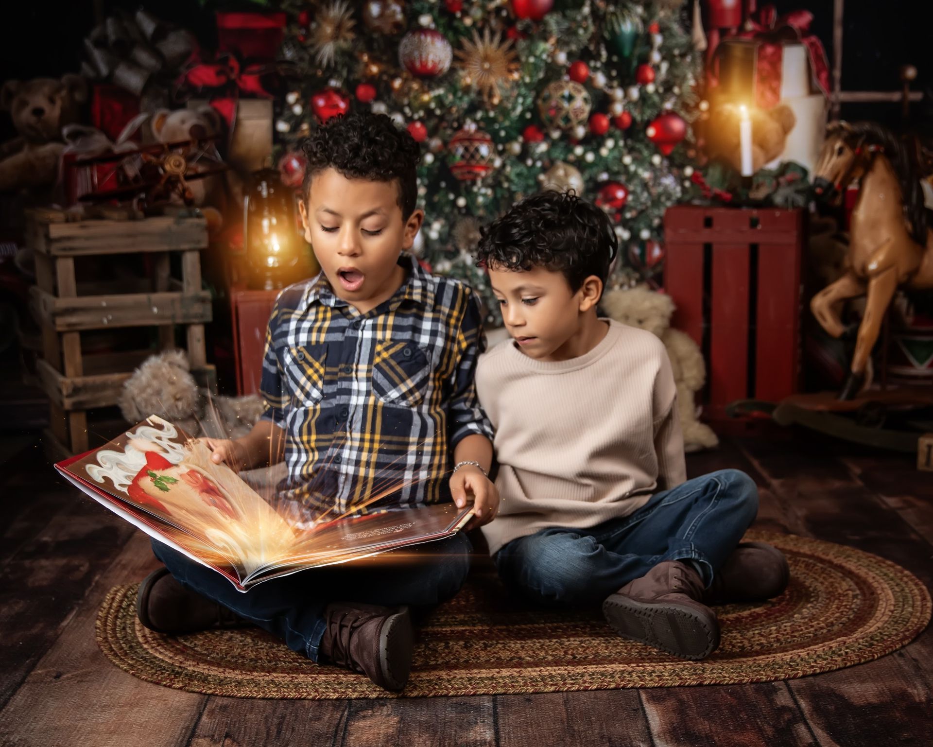 Two young boys are sitting on the floor reading a book in front of a christmas tree.