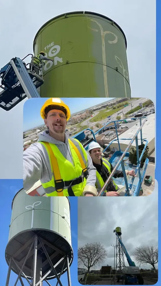 Water tower being worked on; workers in safety gear, boom lift. Green tower, blue sky.