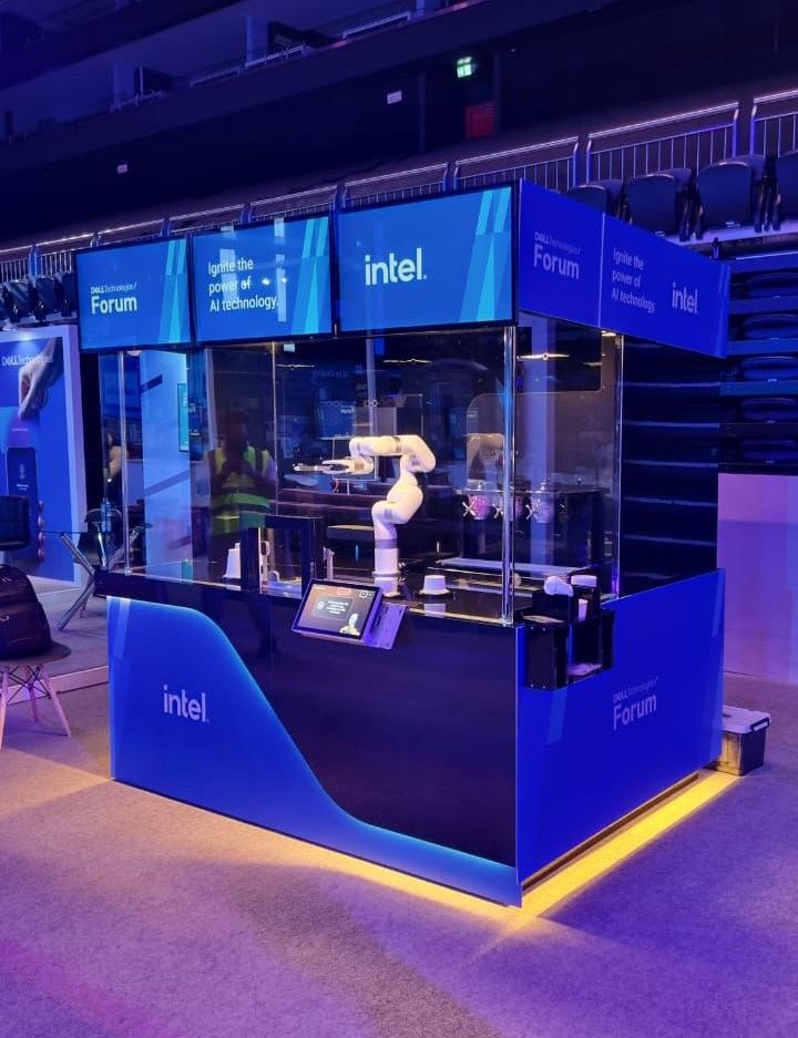 An Intel kiosk with a robotic arm making drinks. Blue and black design with Intel logo and displays.