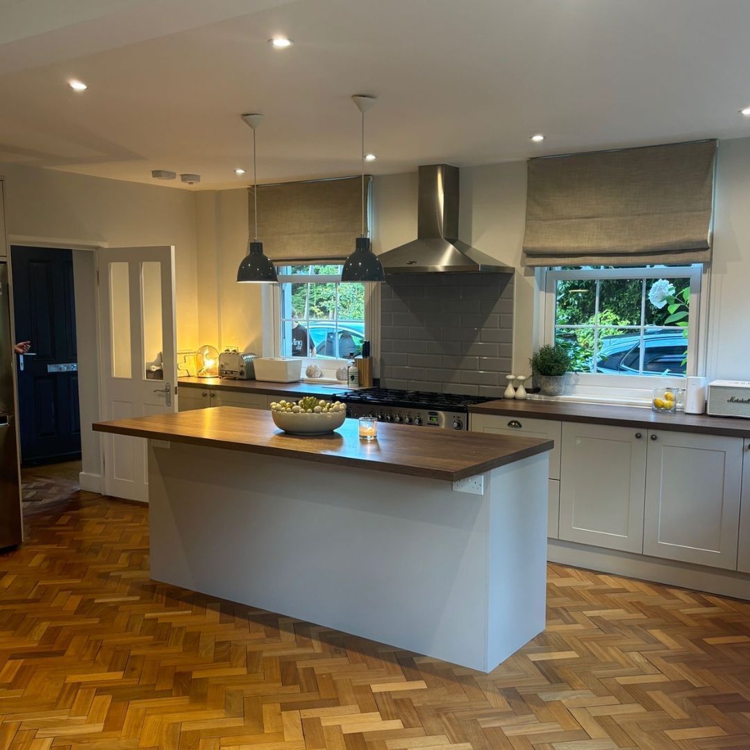 Kitchen with white cabinets, wood island, and parquet flooring. Roman shades cover windows.