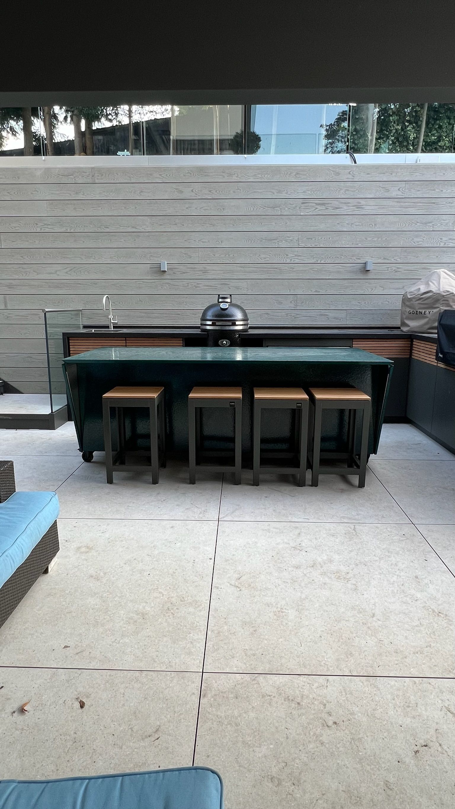 Patio with a dark-green bar, stools, and a grill, set against a stone wall.