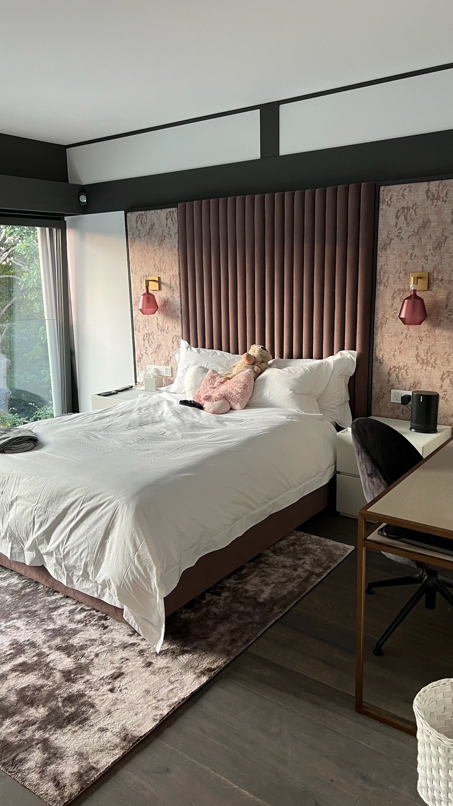 Bedroom with bed, desk, and rug. Pink headboard, white bedding. Window left.