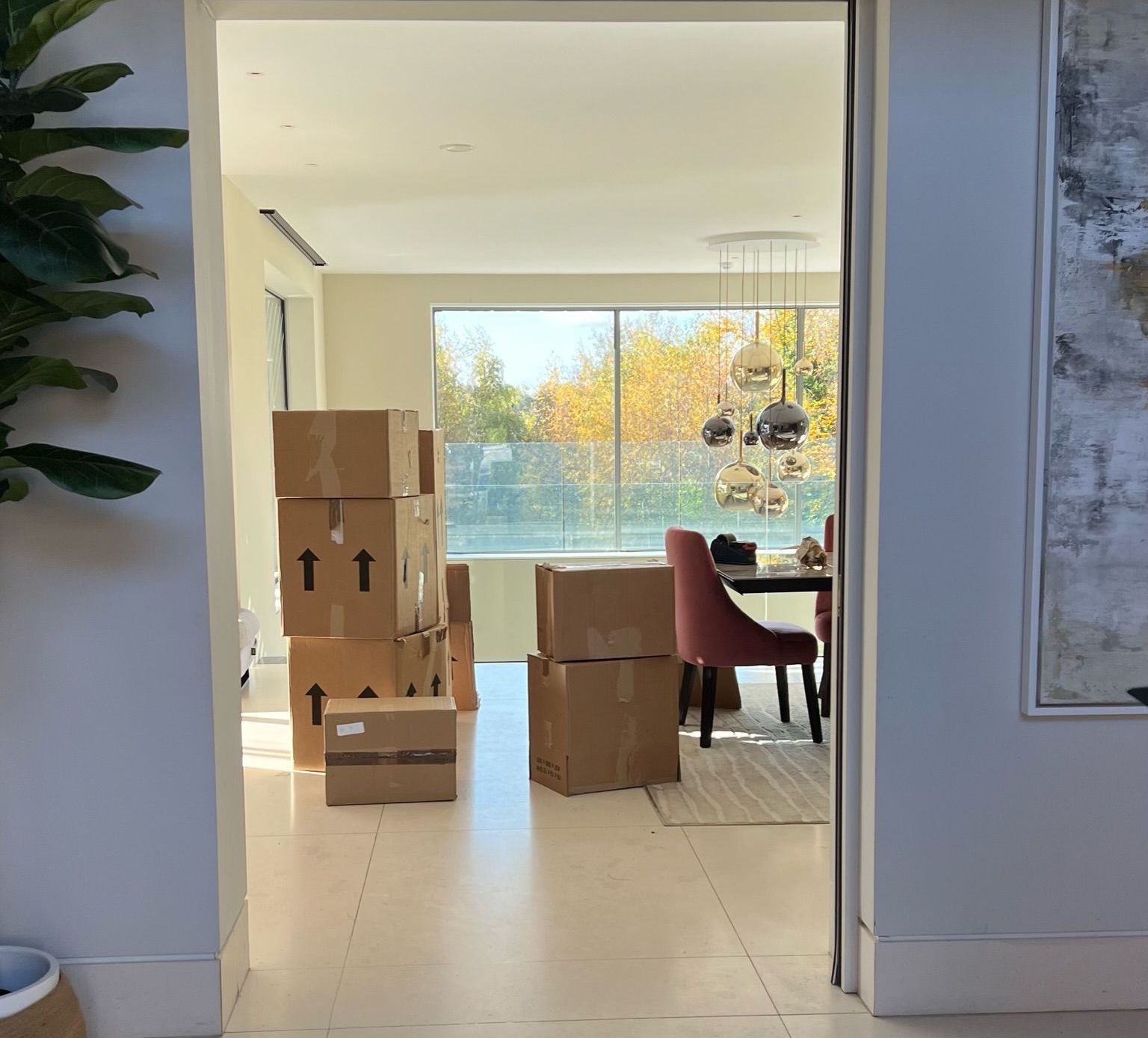 Boxes stacked in an entryway, leading to a dining room with a window and a table setting.