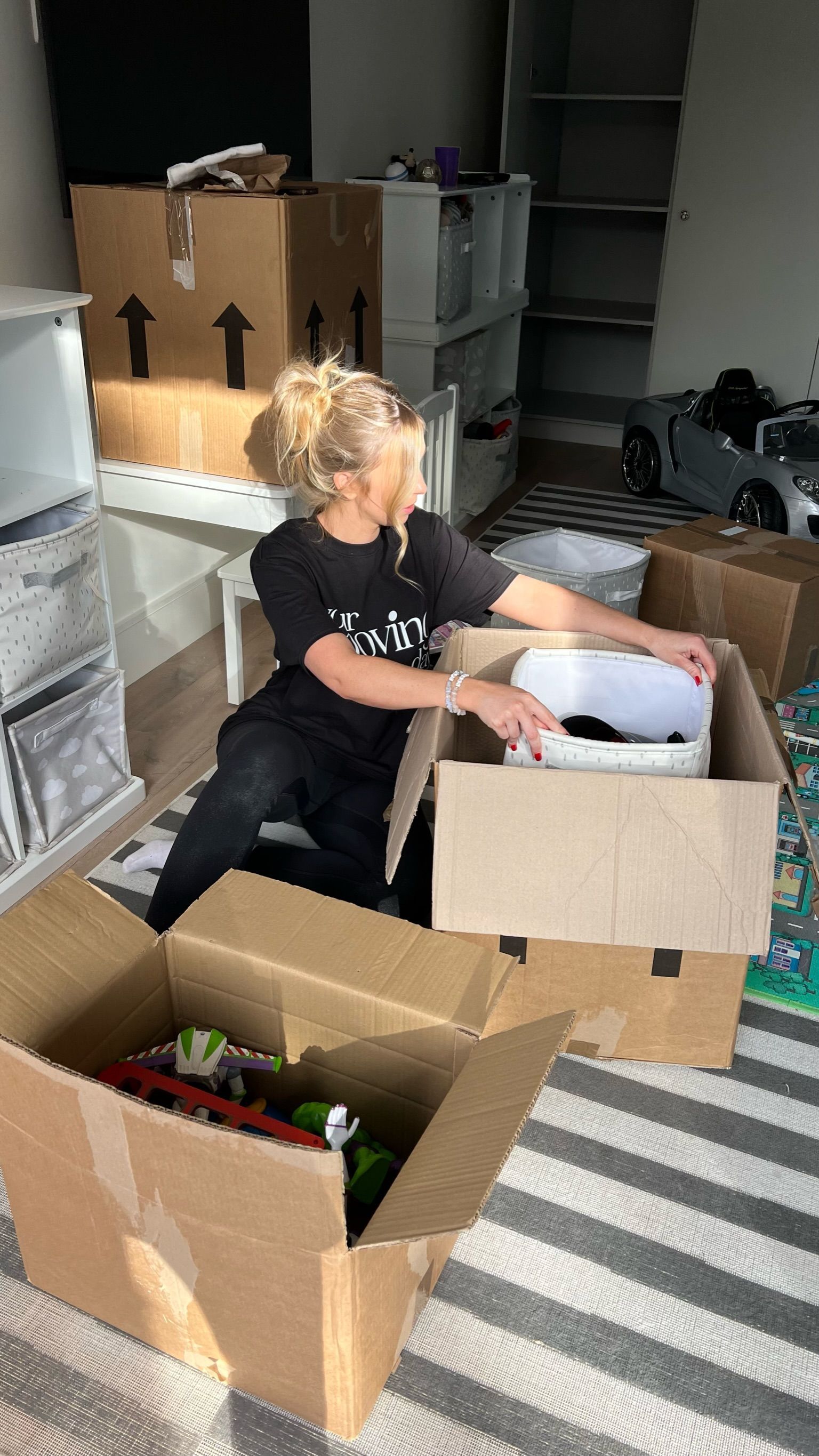 Woman unpacking boxes in a room with shelves, possibly moving.
