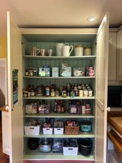 A pantry cabinet filled with food items and kitchenware; shelves are organized and neatly arranged.