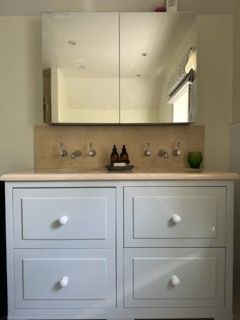 Bathroom vanity with gray drawers, wooden countertop, mirrored cabinet, and sink fixtures.
