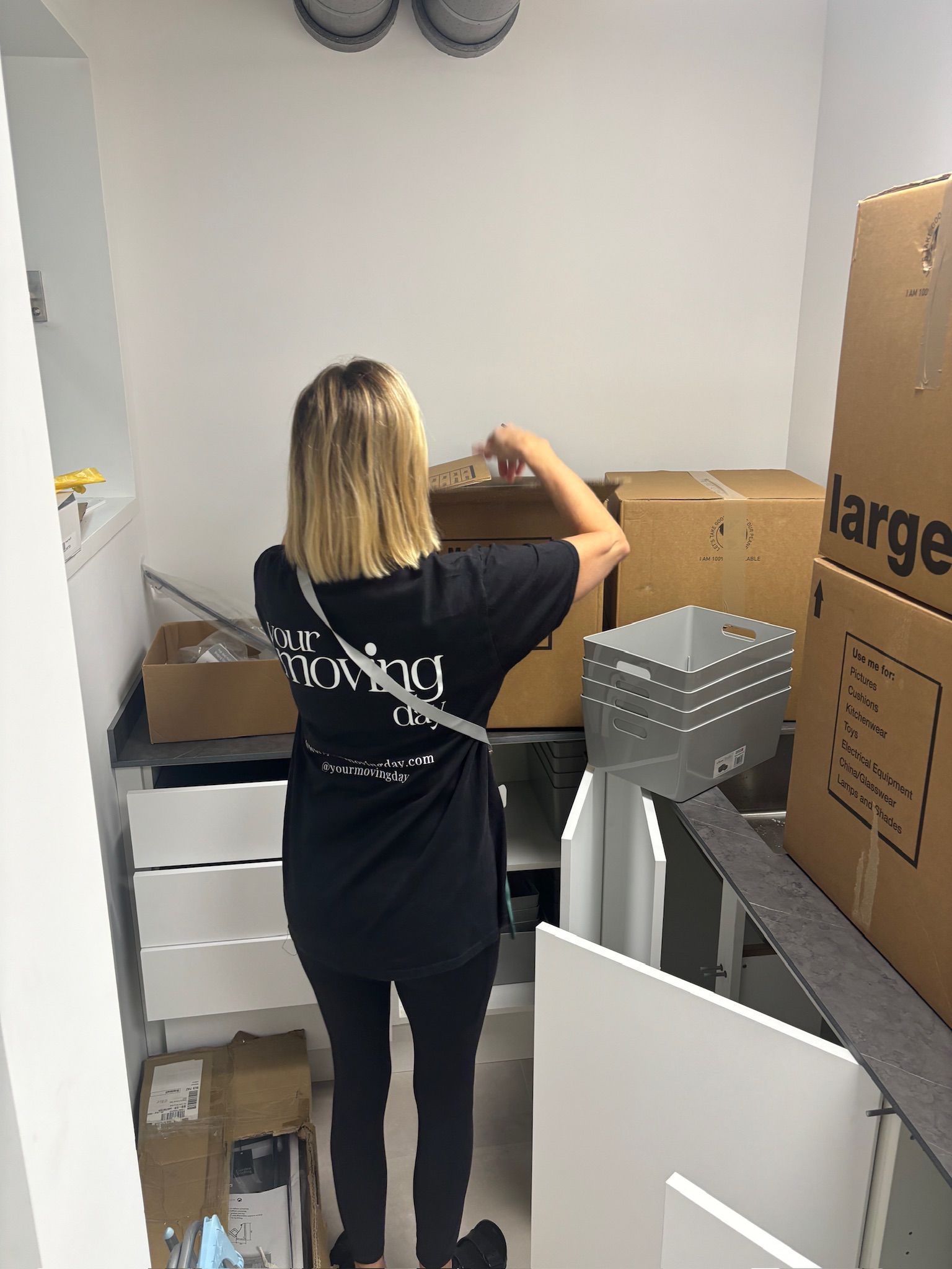 Woman in black shirt and pants packs boxes inside a small, white room.