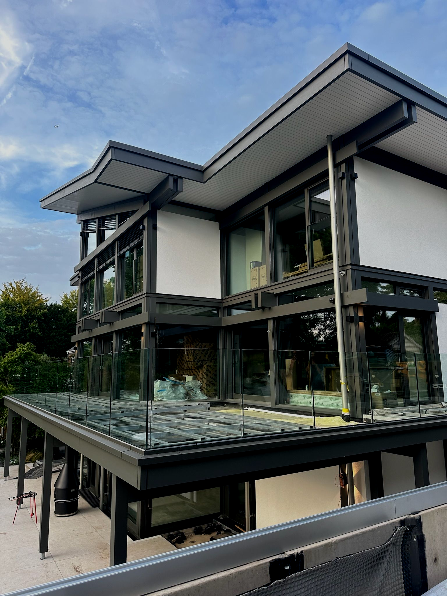 Modern house with glass walls, dark trim, and a flat roof against a cloudy sky.