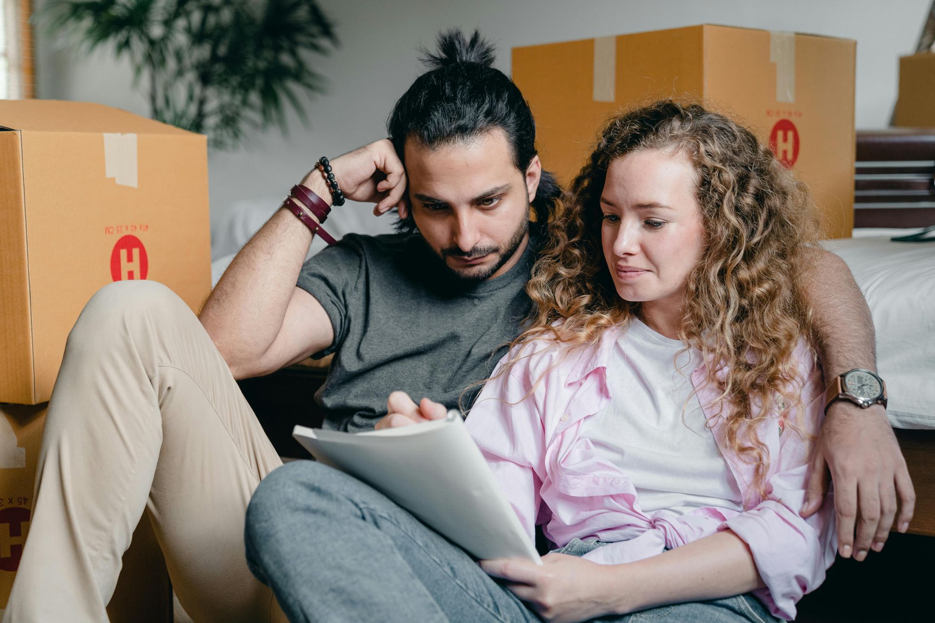 Couple sitting on floor, looking at document, surrounded by moving boxes.