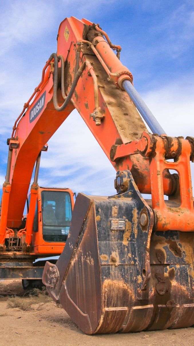 A large orange excavator is sitting on top of a dirt field.