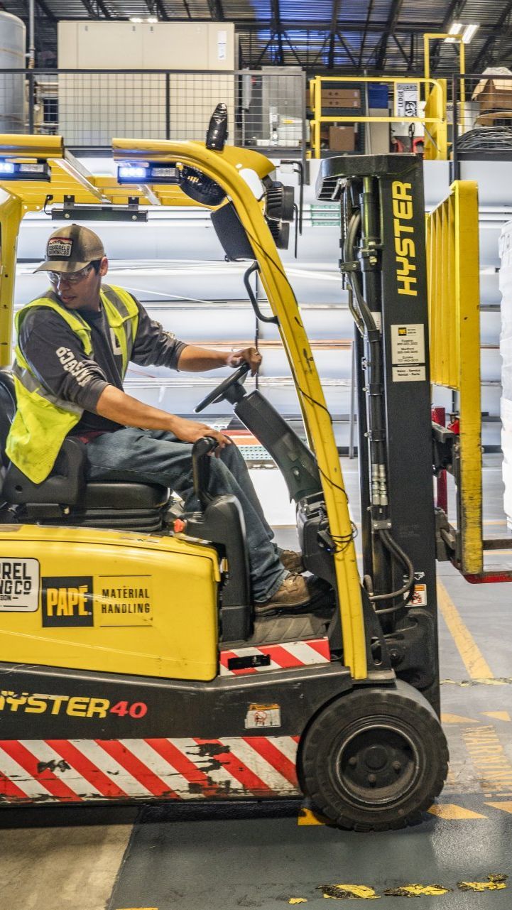 A man is driving a yellow forklift in a warehouse.