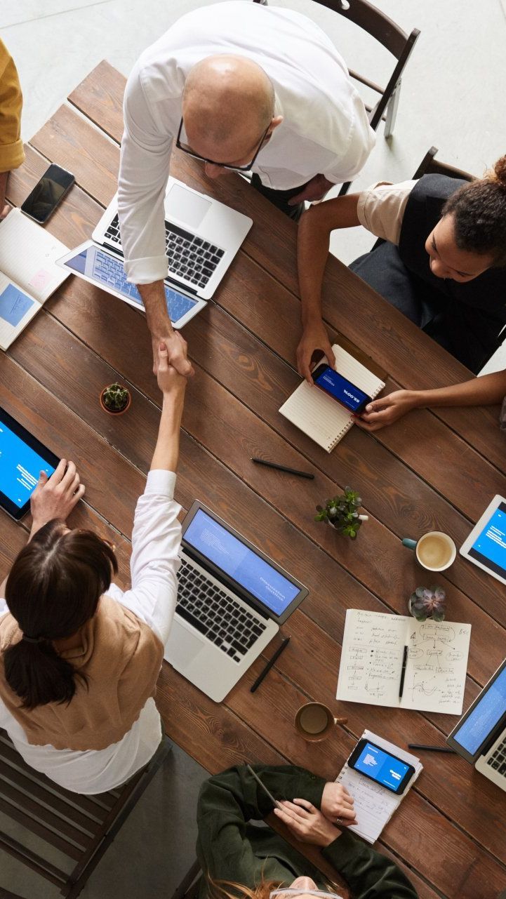 A group of people are sitting around a wooden table shaking hands.