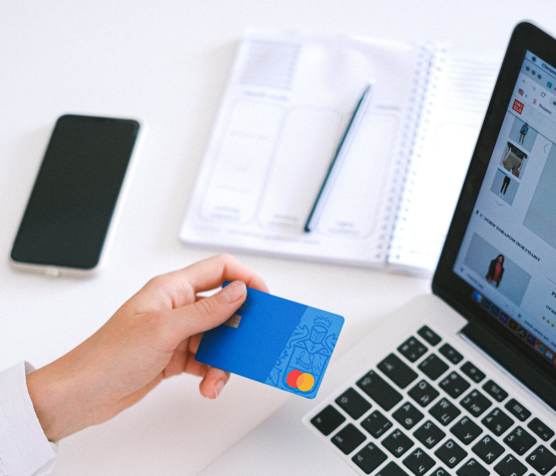 A person is holding a credit card in front of a laptop