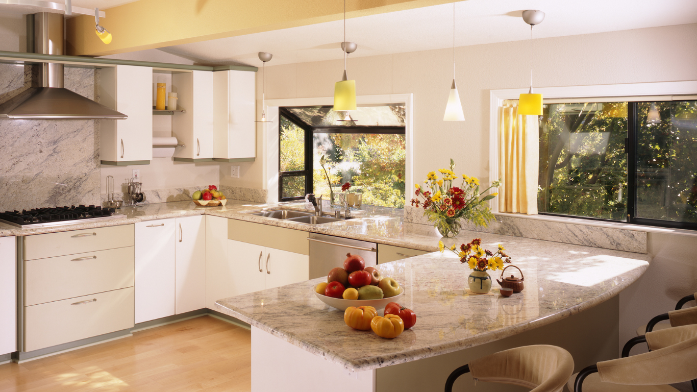 Bright modern kitchen with white cabinets, granite island, fruit bowl, and large sunlit windows