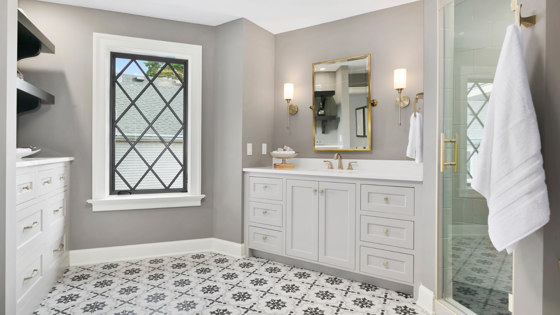 Bright bathroom with patterned black-and-white tile, white vanity, mirror, and shower with a towel