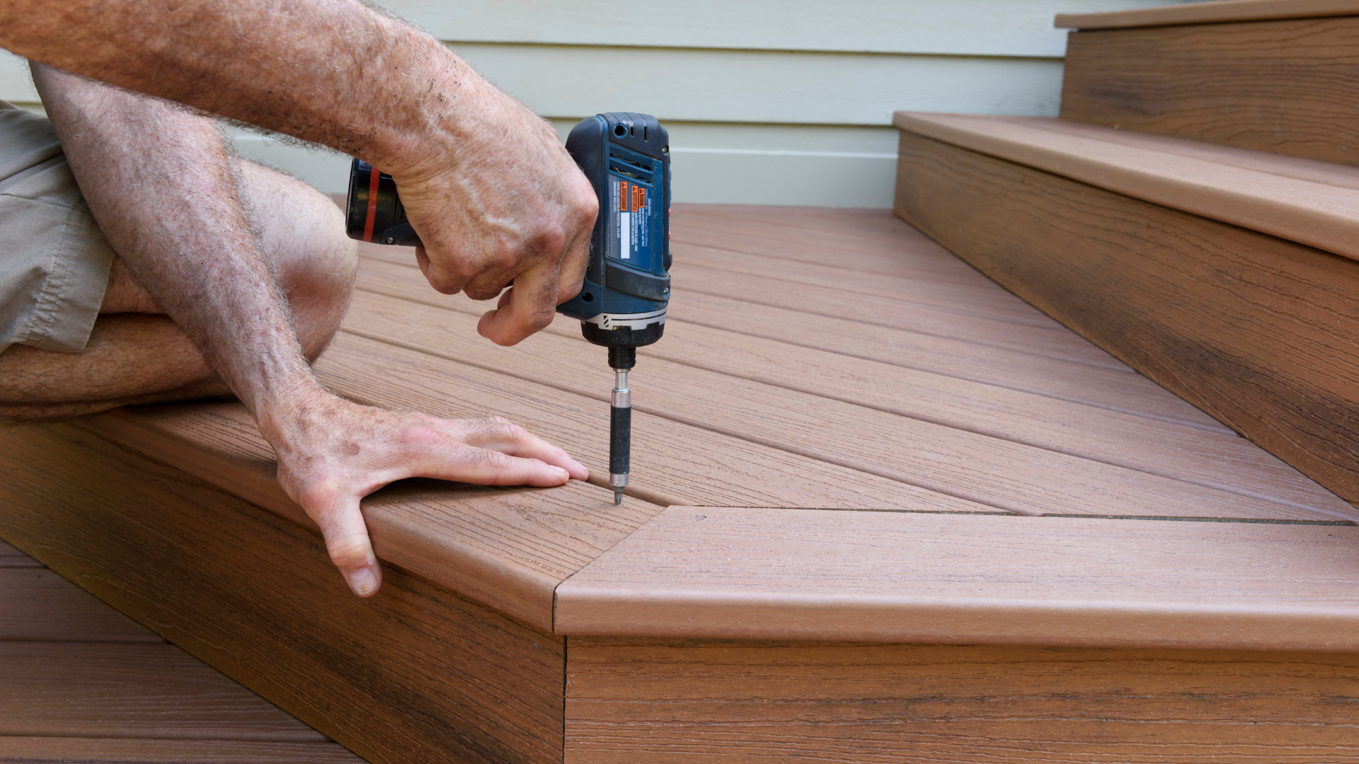 Person using a drill to fasten wood decking boards on an outdoor step.