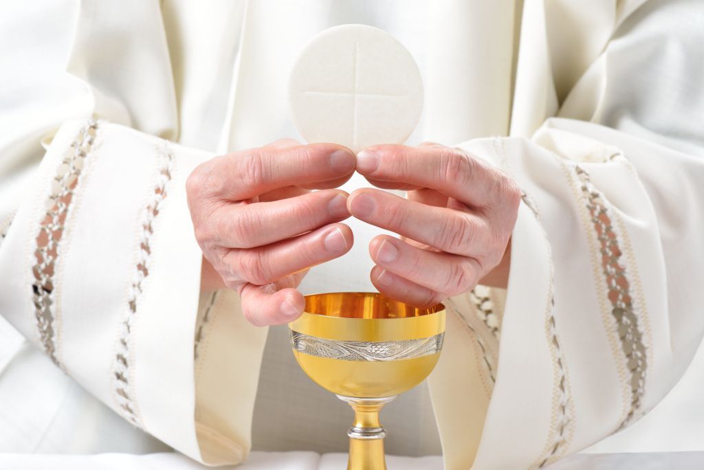 Priest holding a white communion wafer and gold chalice during Mass