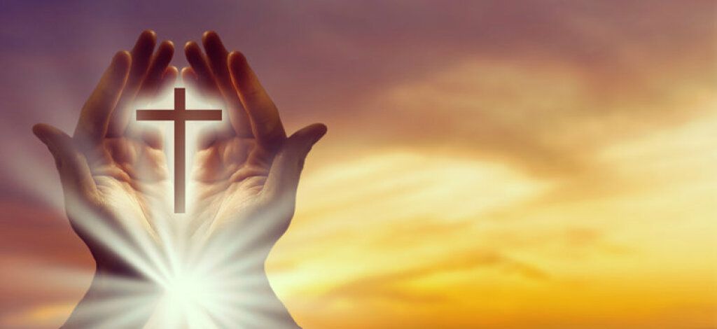 Hands raised around a glowing cross at sunset sky