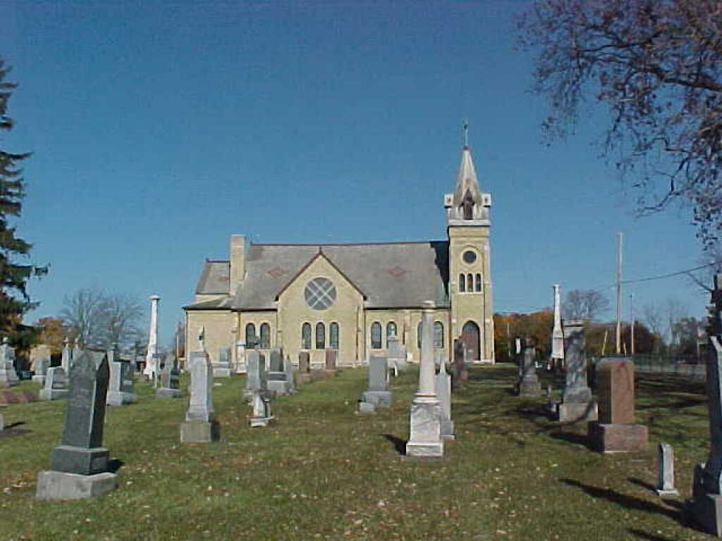 Church with tall steeple in a cemetery, viewed on a clear day with gravestones in the foreground