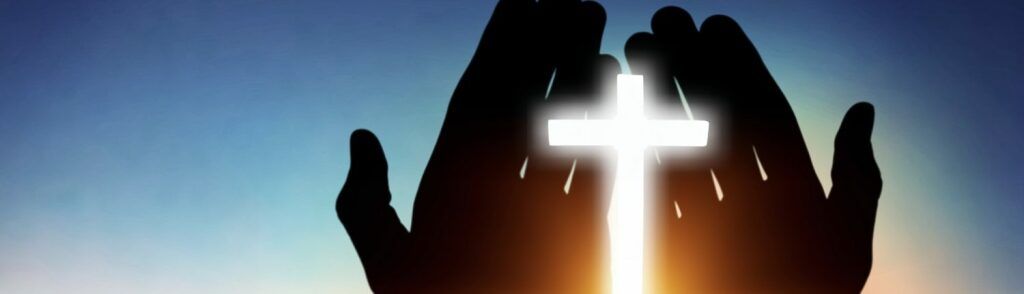 Silhouetted hands framing a glowing cross against a blue sunset sky
