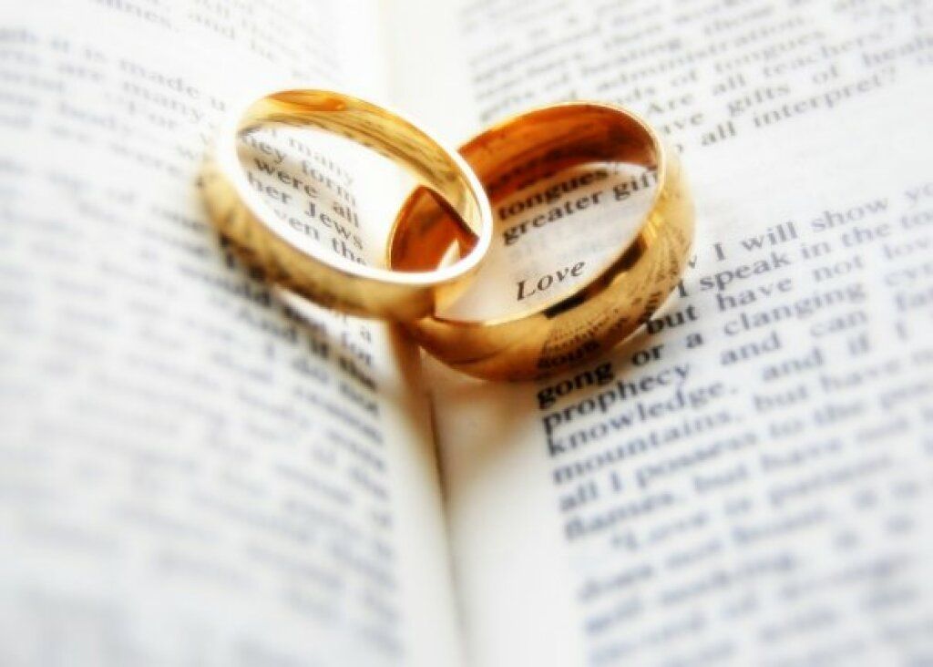 Two gold wedding rings resting on an open book, one engraved “Love”