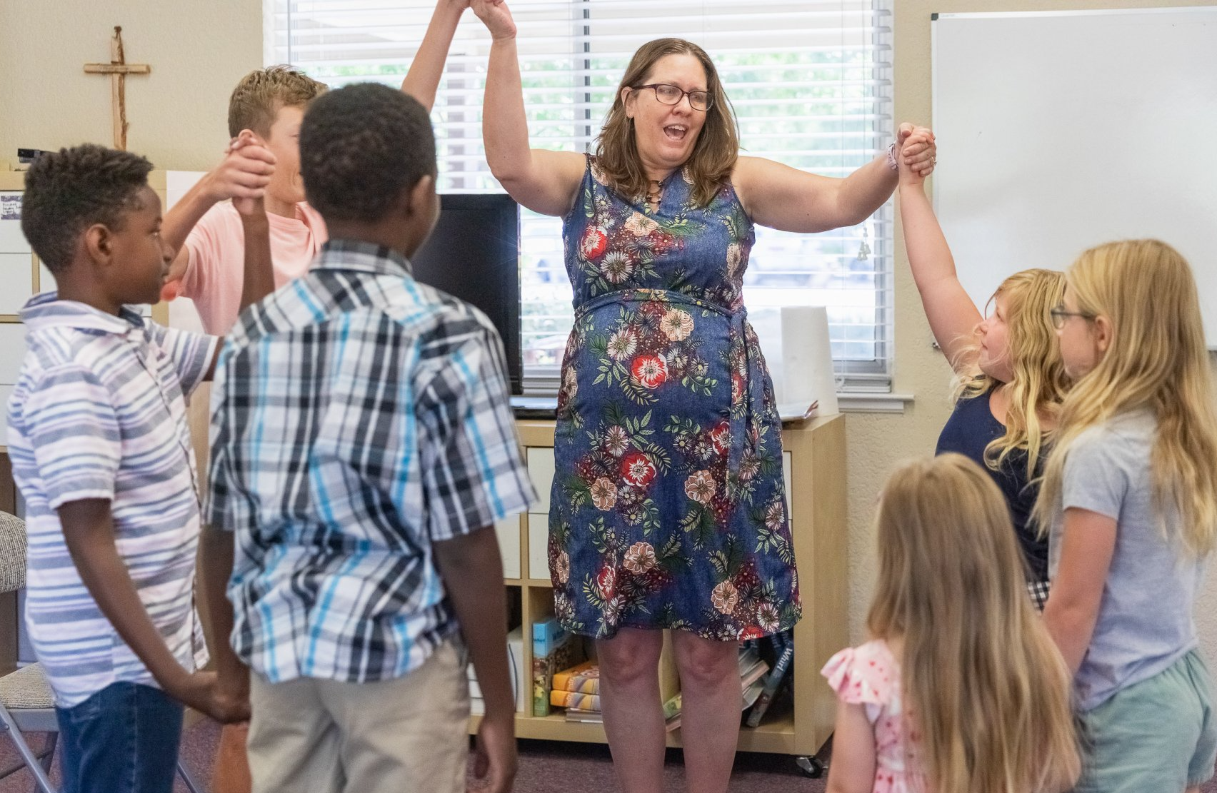 A woman is standing in a circle of children holding hands.