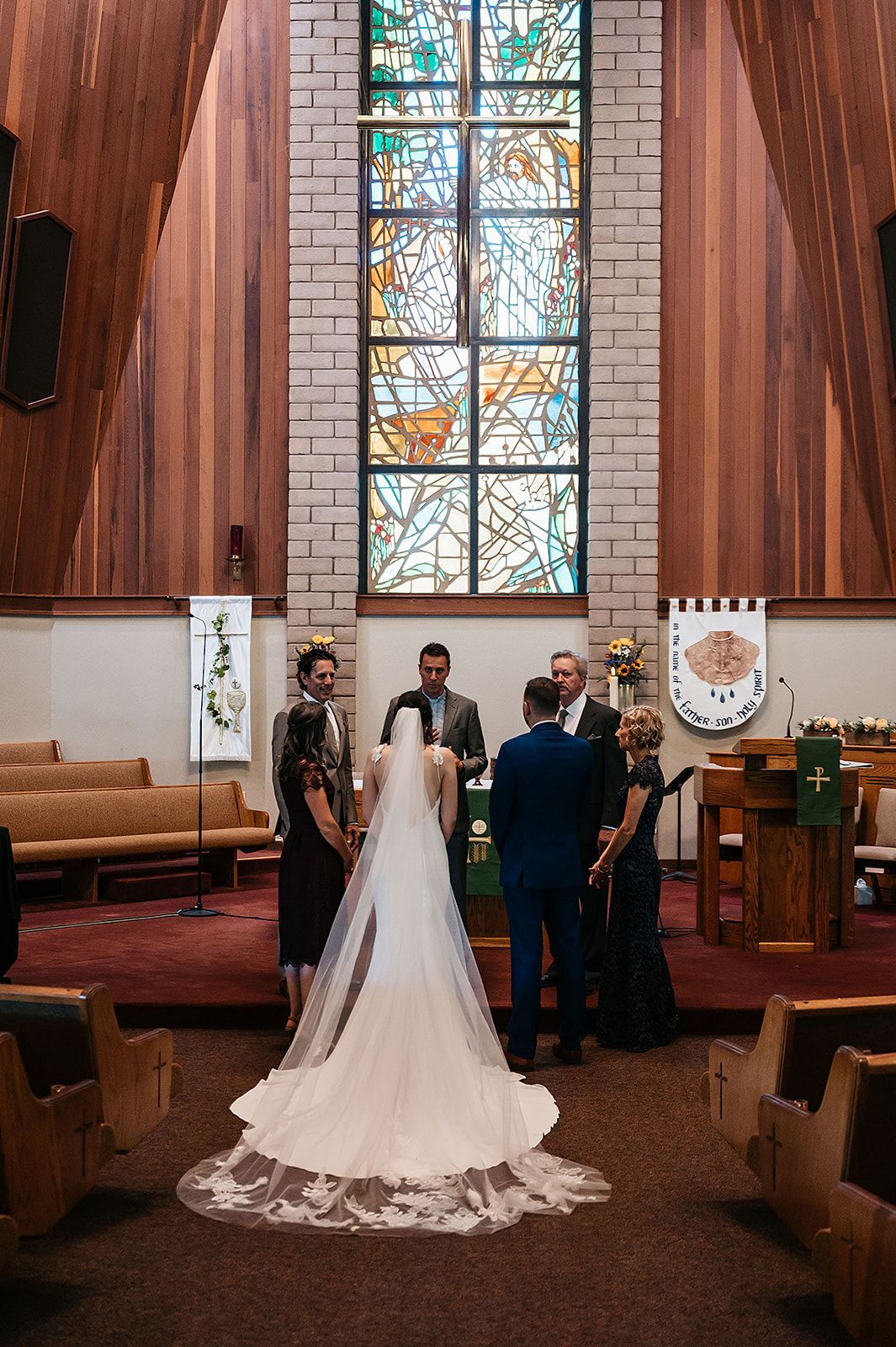 A bride and groom are getting married in a church in front of a stained glass window.