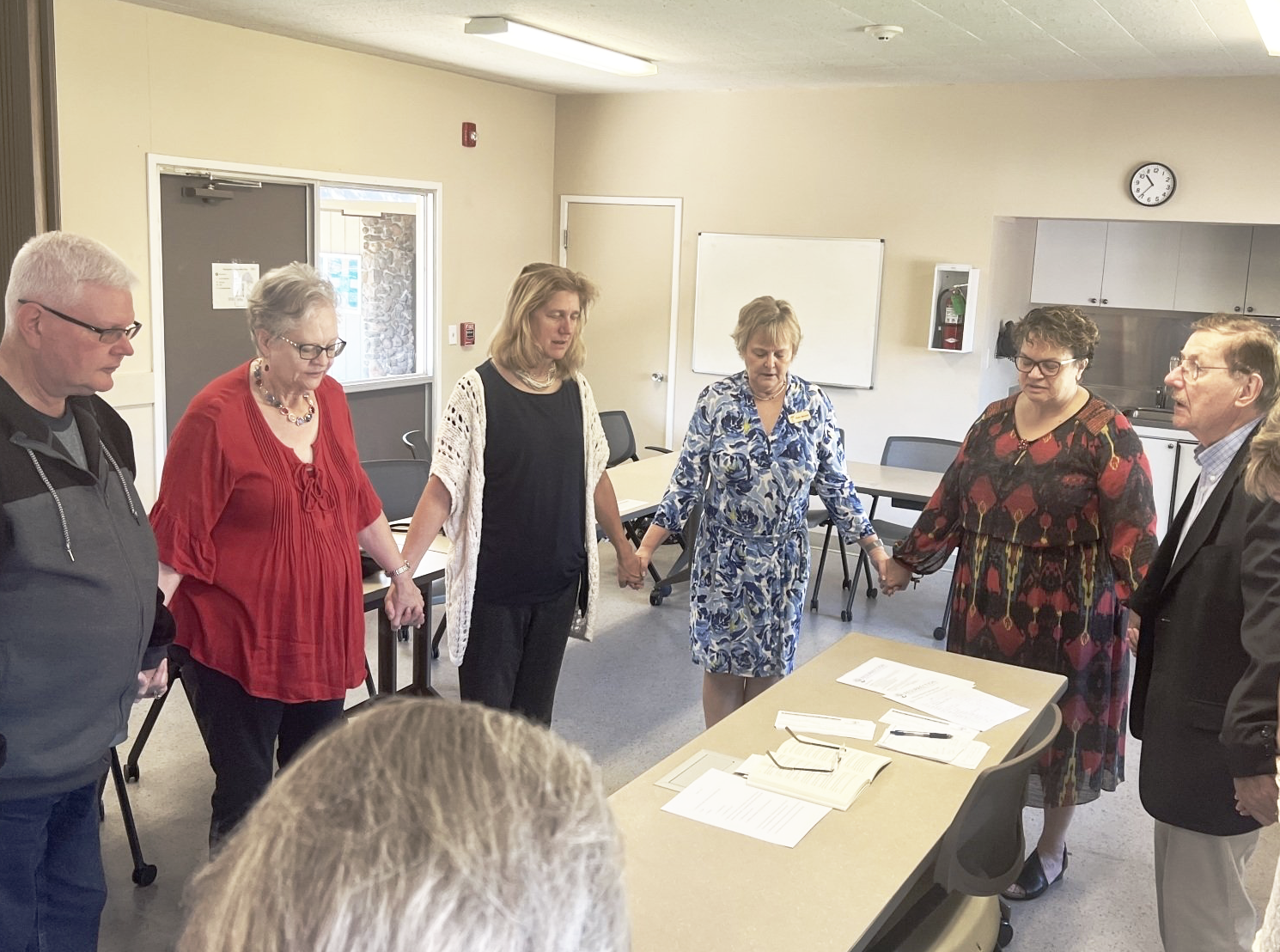A group of people are standing around a table holding hands.
