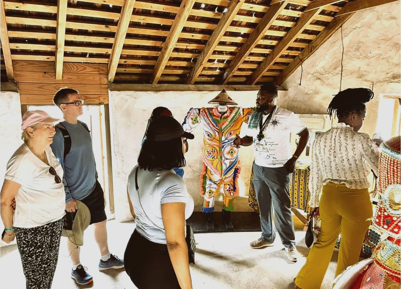 Group of people in a room, looking at colorful display. Wooden ceiling, display features artistic clothing.