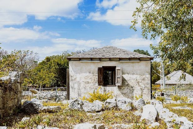 Small, weathered building with open window in a rocky field under a blue, cloudy sky.