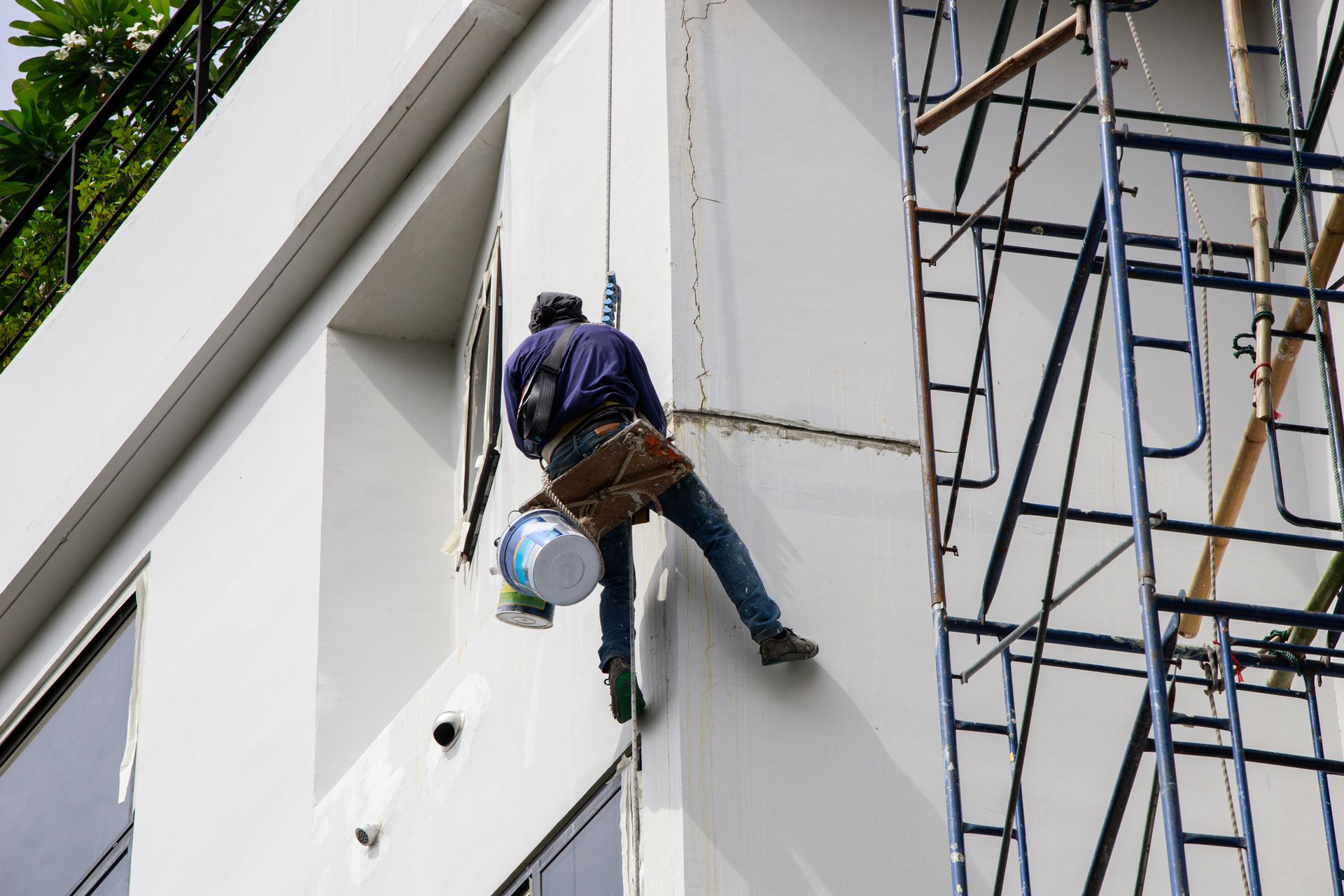 A man is climbing up a building with a bucket of paint.