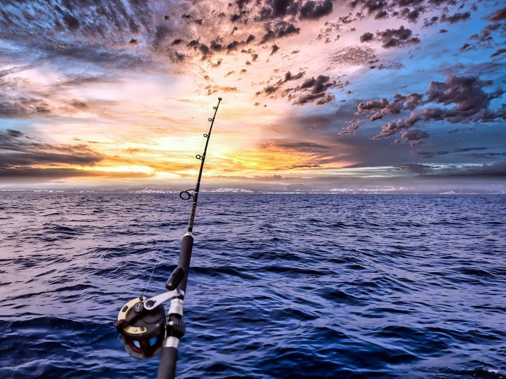 Fishing rod cast over rippling ocean under a colorful sunset sky.