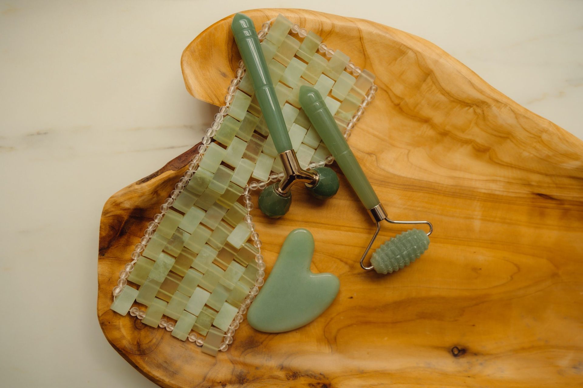 A wooden tray with a jade roller and gua sha on it.