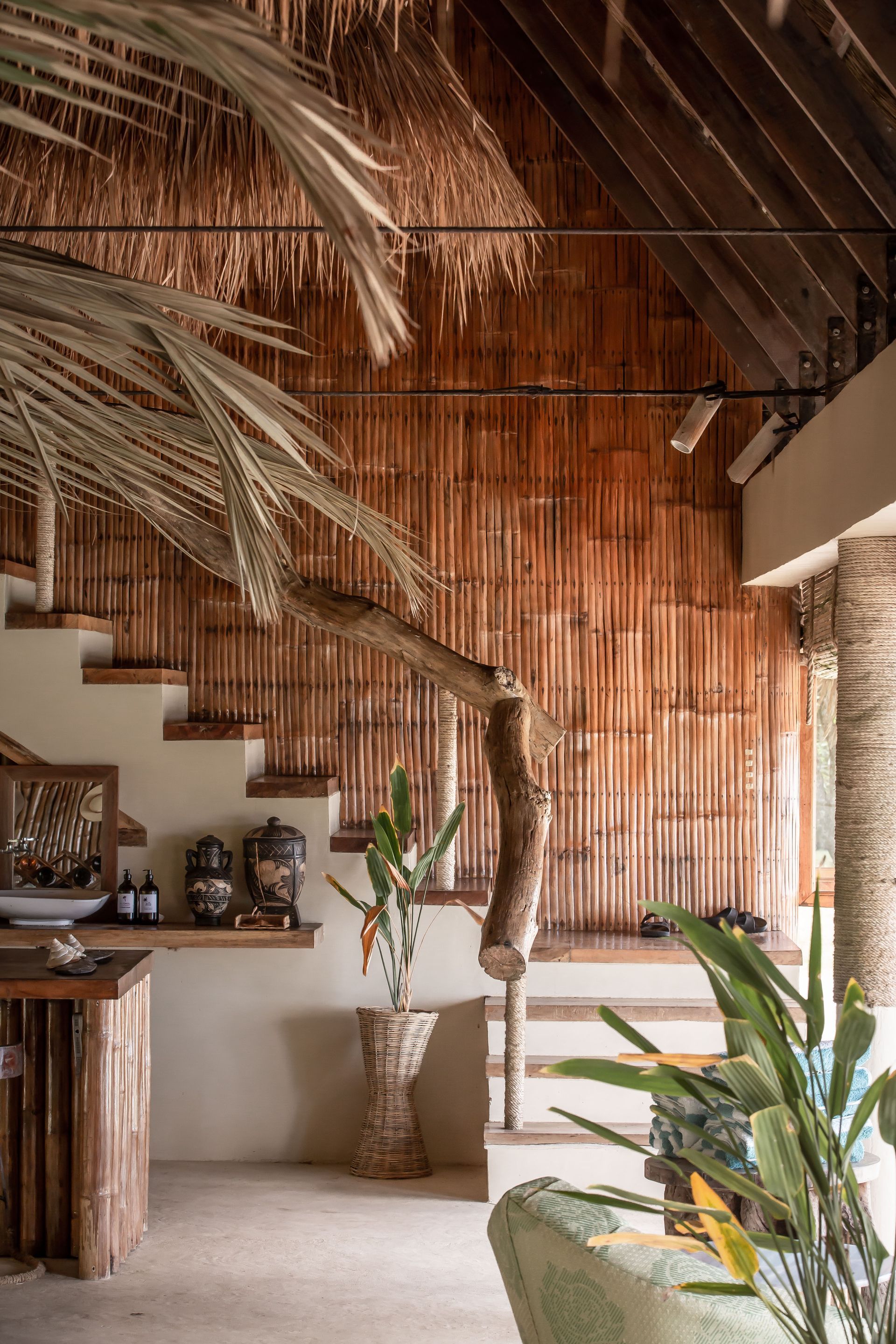 A living room with a wooden staircase and a thatched roof.