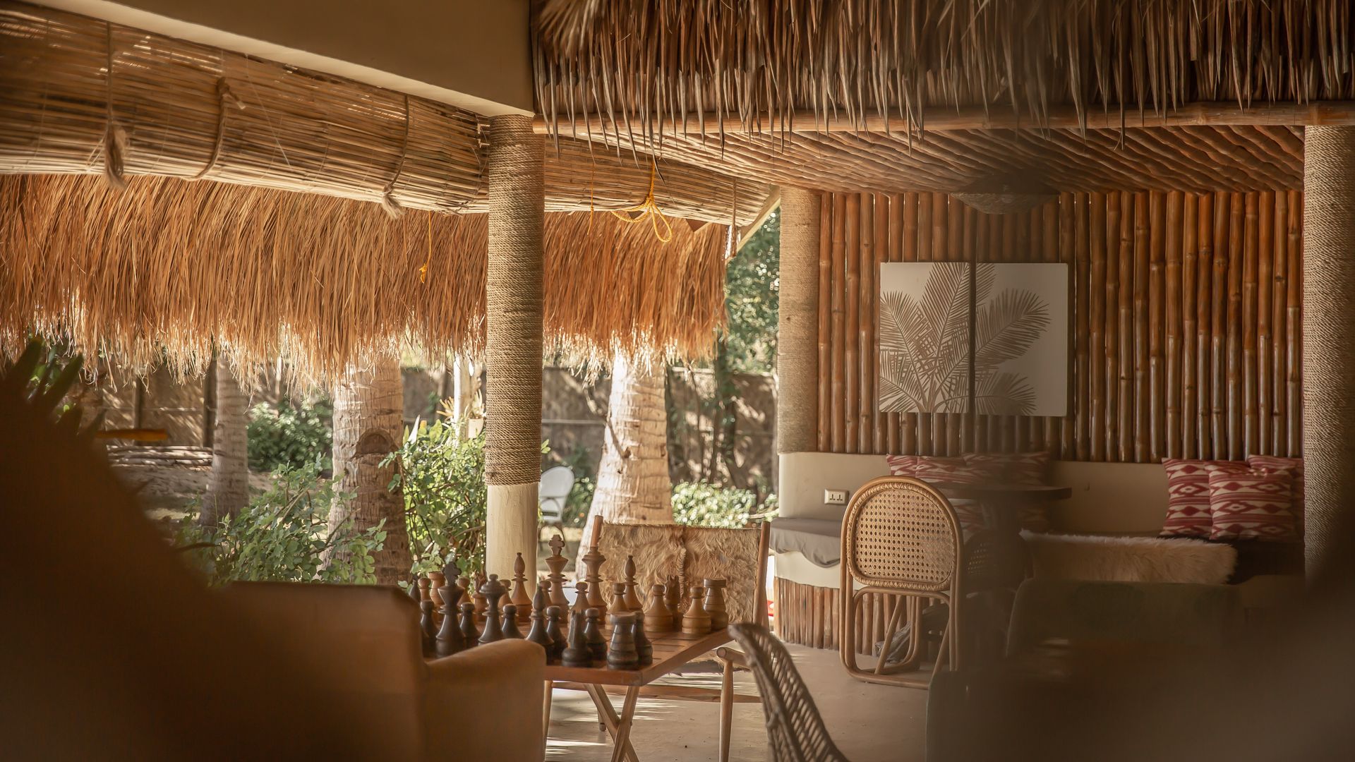 A room with a table and chairs under a thatched roof.