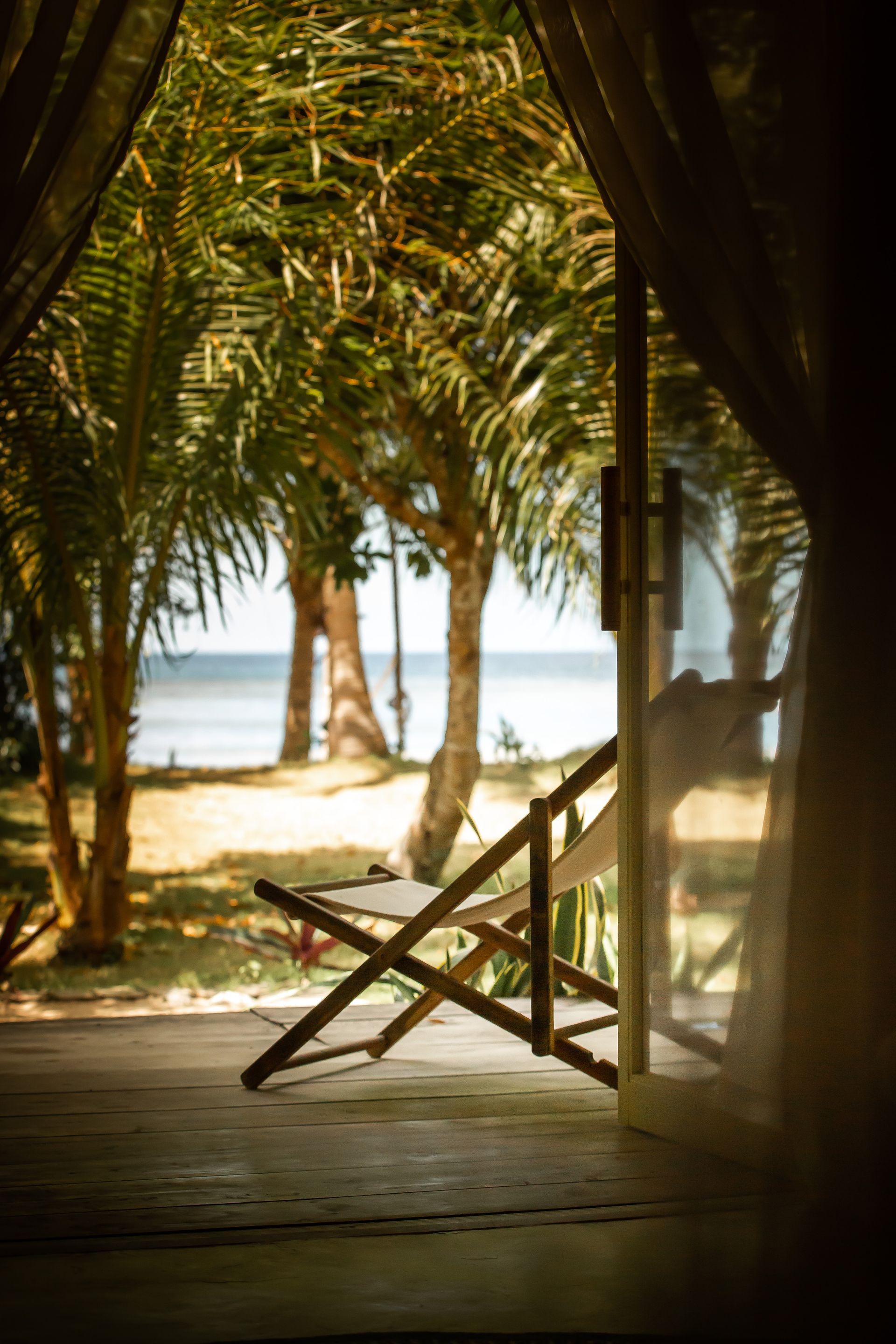 A view of the ocean from a tent with a chair and trees.