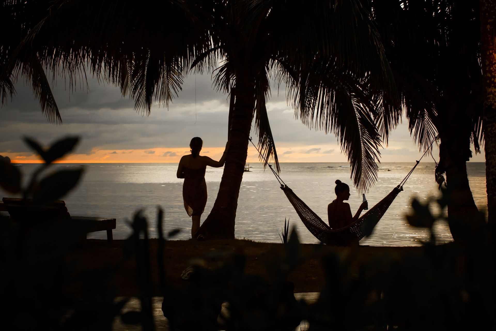 A man is standing next to a woman in a hammock on the beach.