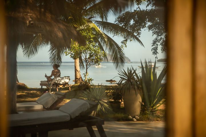 A woman is sitting on a lounge chair near the ocean.
