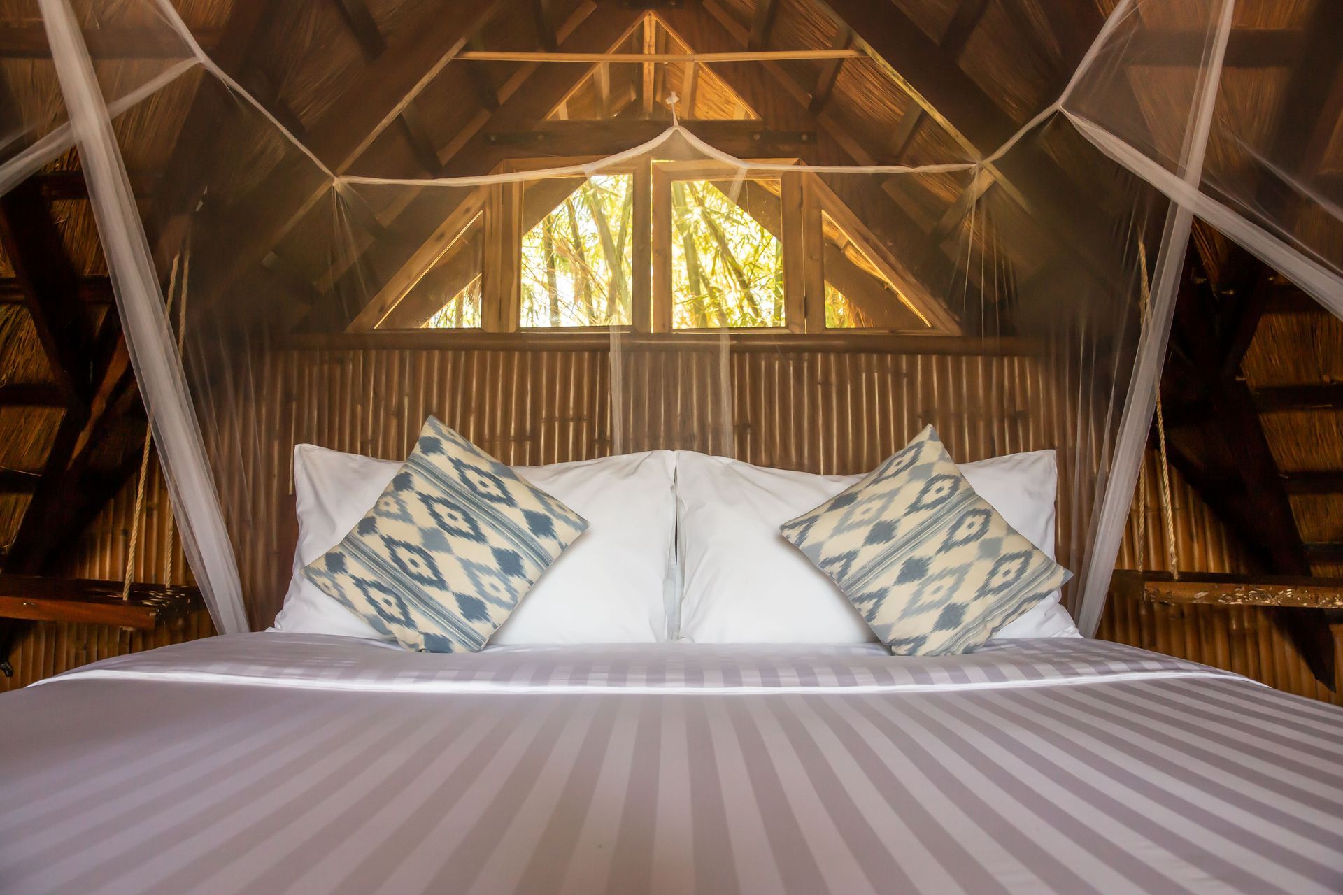 A bed with white sheets and pillows under a mosquito net in a hut.