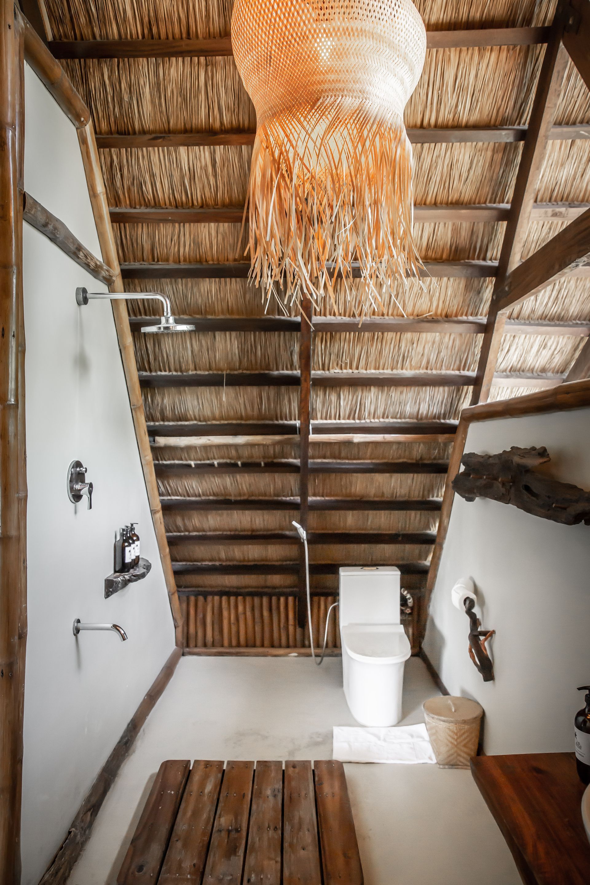 A bathroom with a thatched roof , a toilet , and a shower.