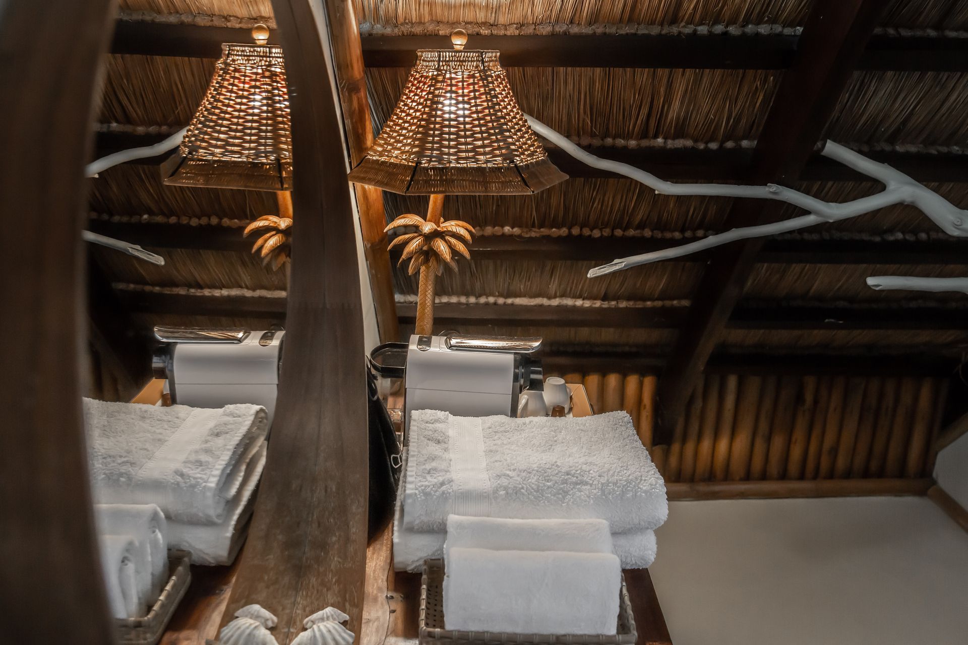 A bathroom with a thatched roof and a stack of towels on the floor.