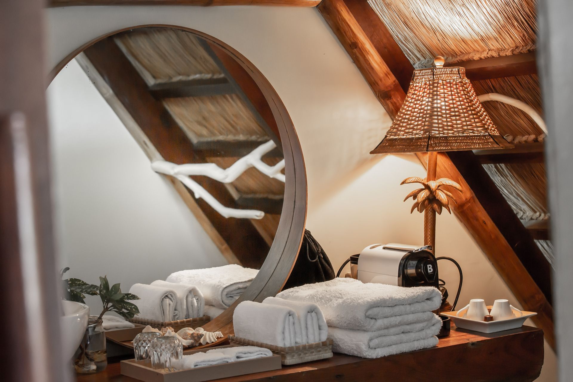 A bathroom with a round mirror , towels and a lamp.